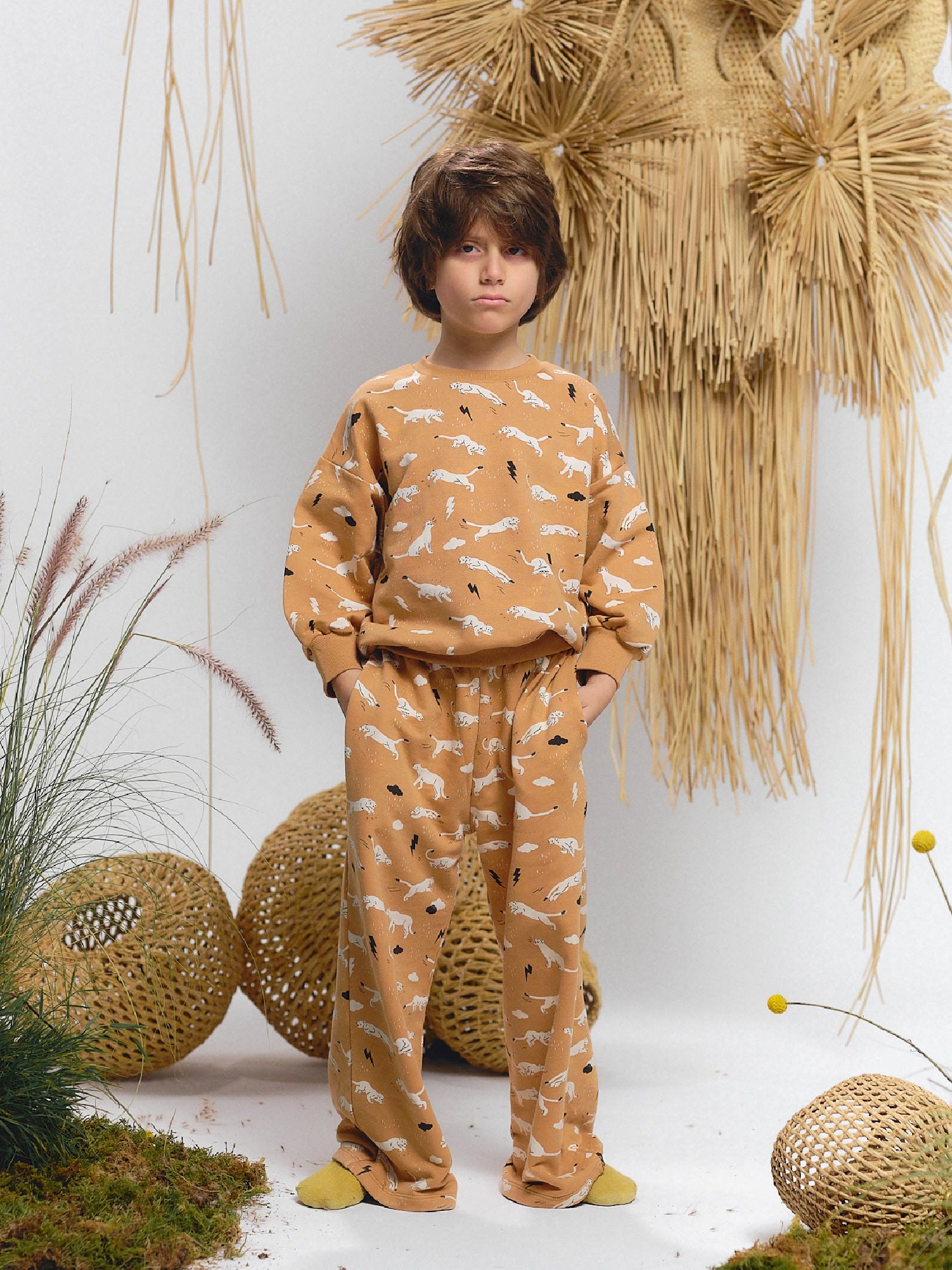 Boy wearing a caramel-colored sweatshirt and matching pants featuring thunder puma print — running pumas with lightning bolts — styled with yellow socks.