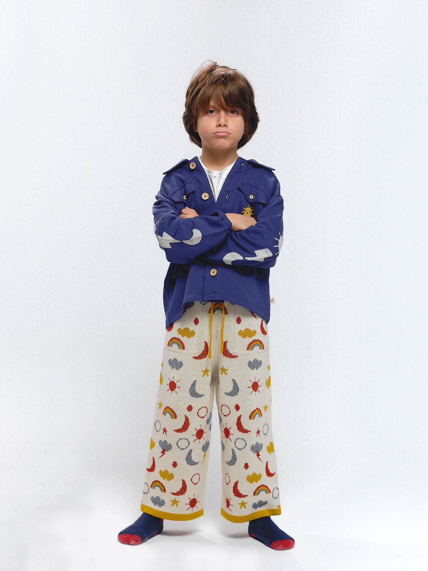 Child in a blue French terry jacket with sky motif prints of sun, moon, and thunder on the sleeves.