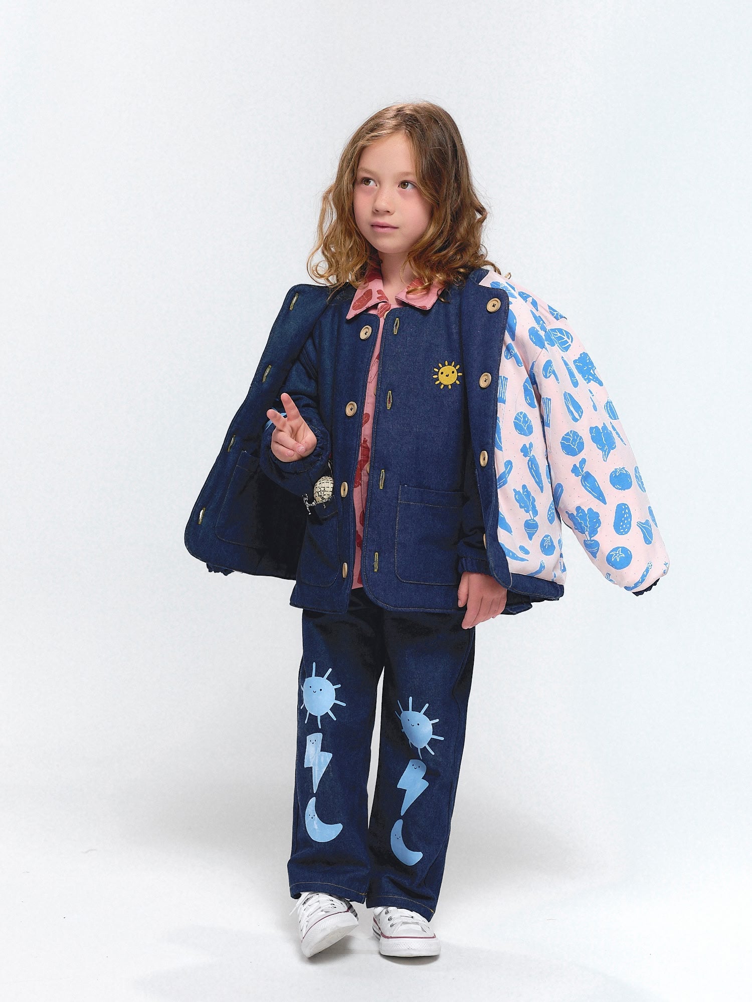 Denim coat and pants decorated with cheerful sky motifs — sun, moon, and thunder — worn over a veggie fiesta inner layer.