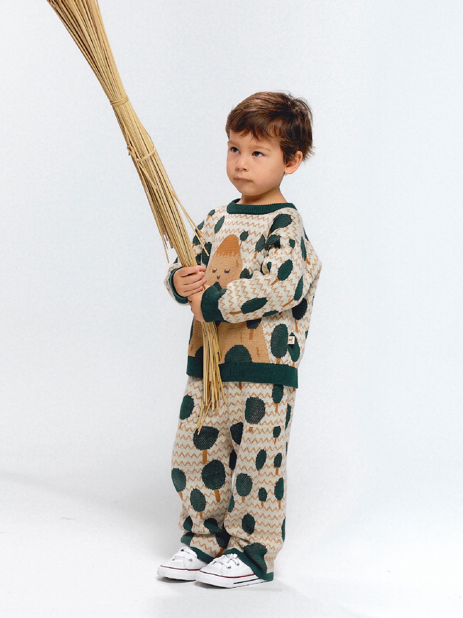 Child wearing a beige jacquard knit set decorated with green tree motifs inspired by mountains.