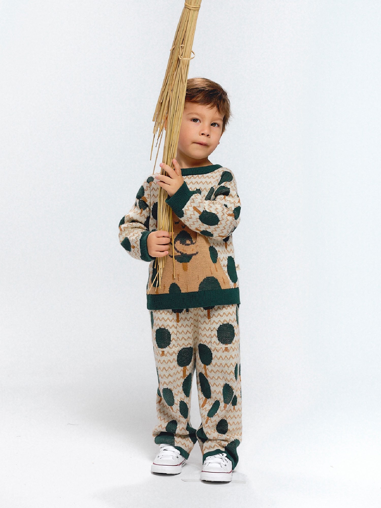 Child wearing a beige jacquard knit set decorated with green tree motifs inspired by mountains.