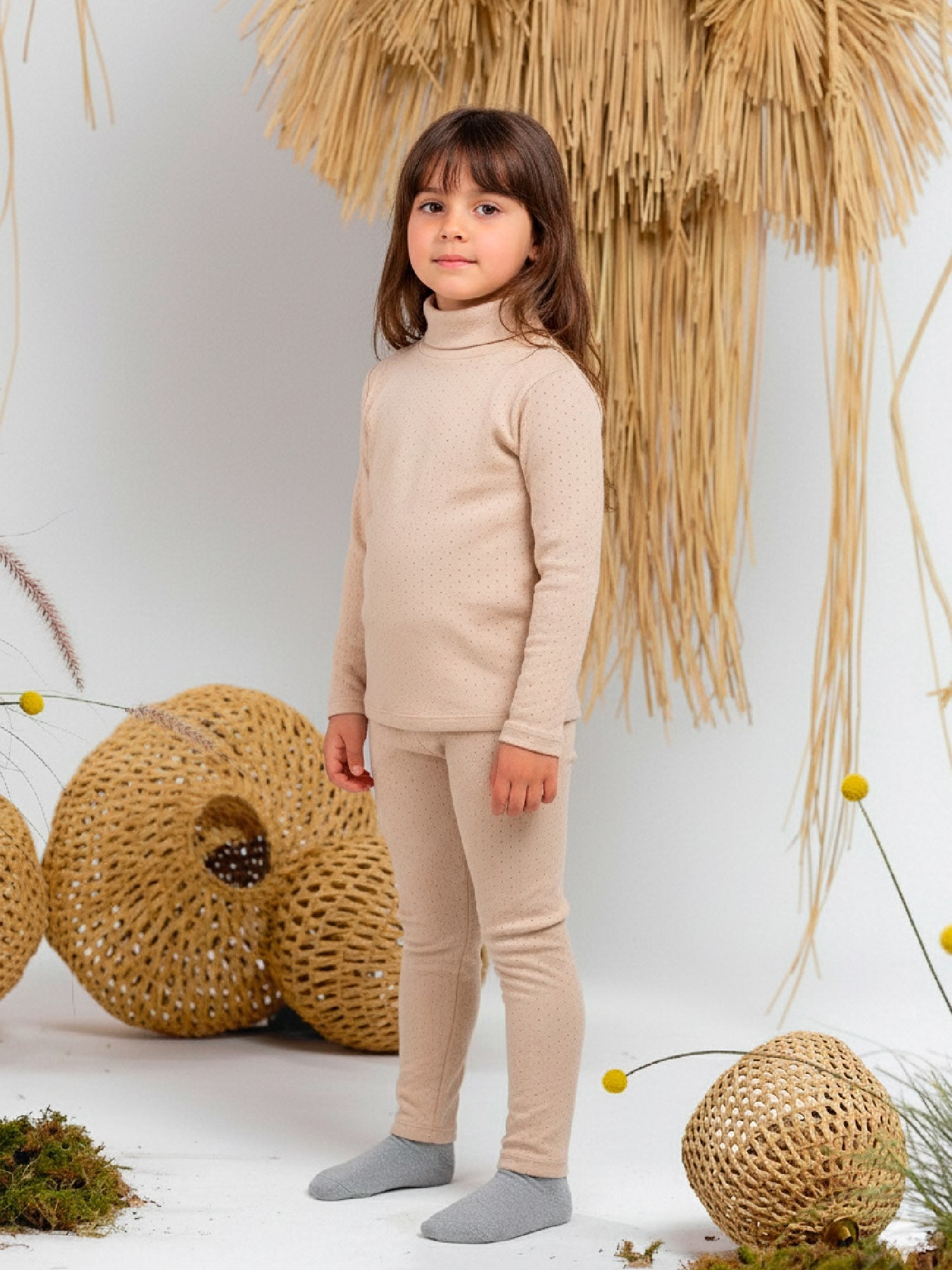 Girl wearing a beige pointelle knit turtleneck top with long sleeves, styled with matching leggings.