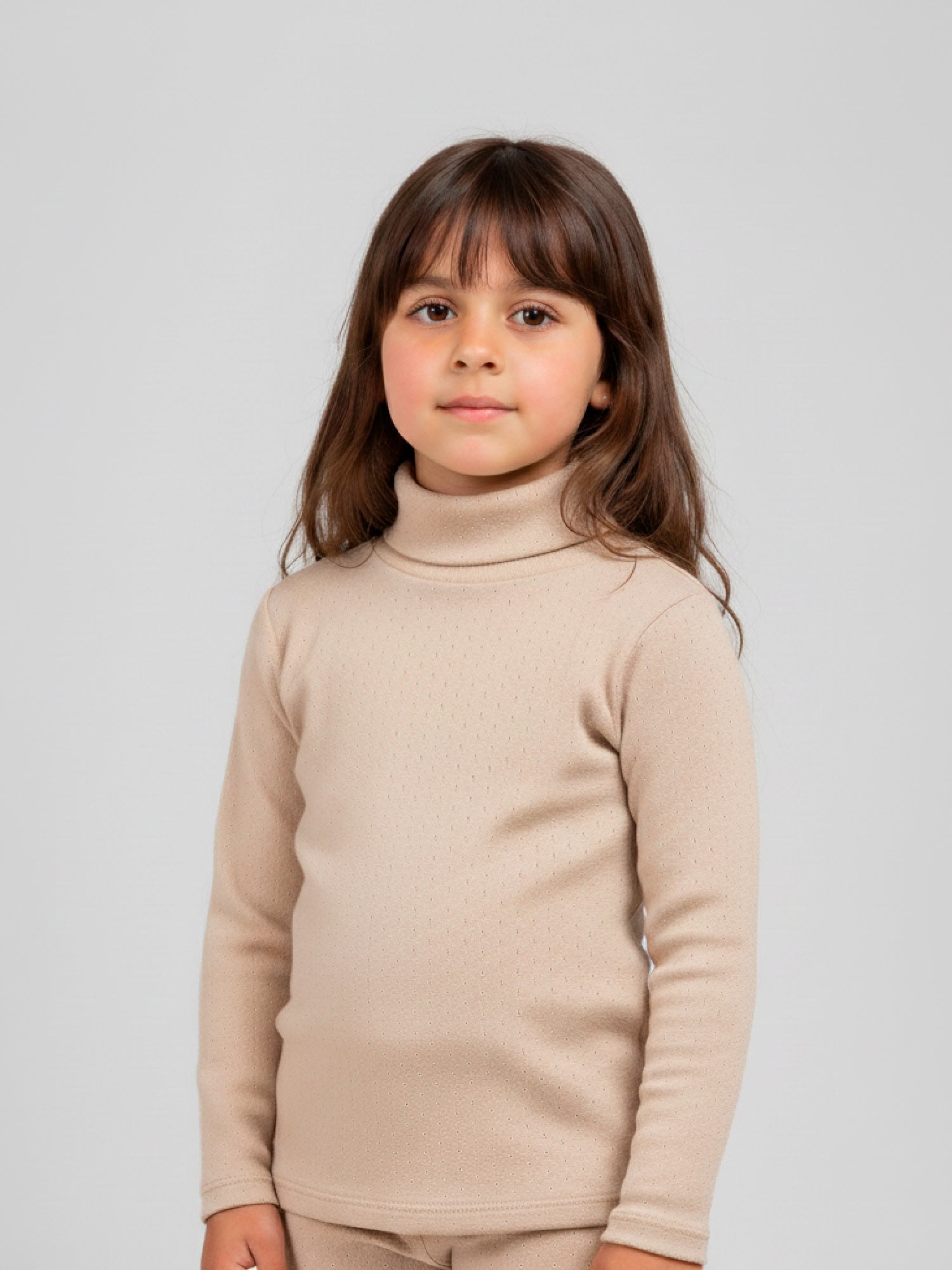 Girl wearing a beige pointelle knit turtleneck top with long sleeves, styled with matching leggings, standing against a neutral background.