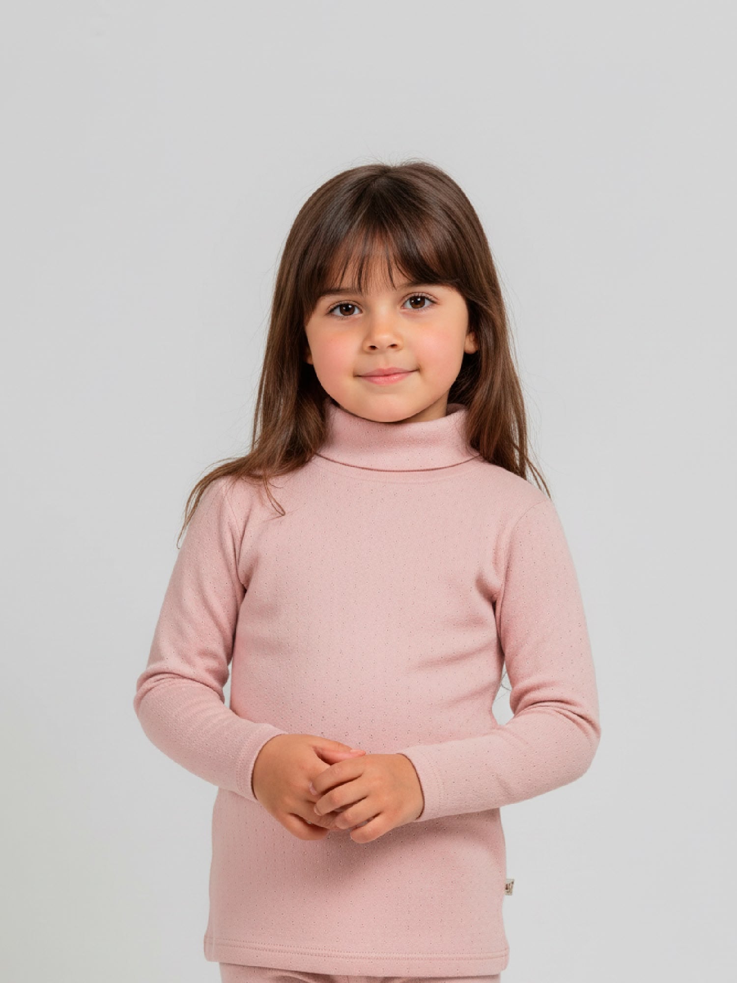 Girl wearing a soft pink pointelle knit turtleneck top with long sleeves, styled with matching bottoms, standing against a neutral background.