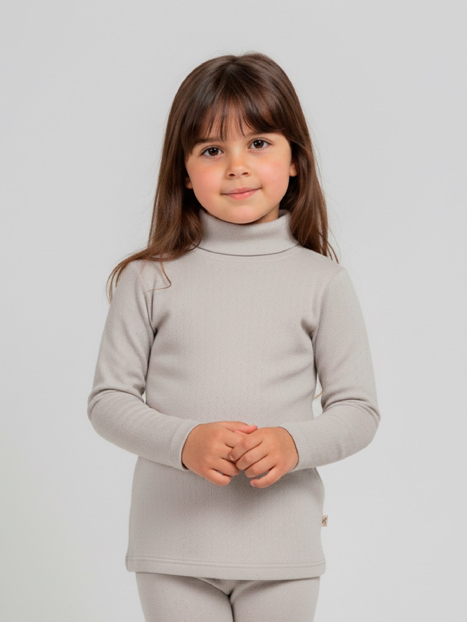 Girl wearing a light gray pointelle knit turtleneck top with long sleeves, styled with matching leggings, standing against a neutral background.