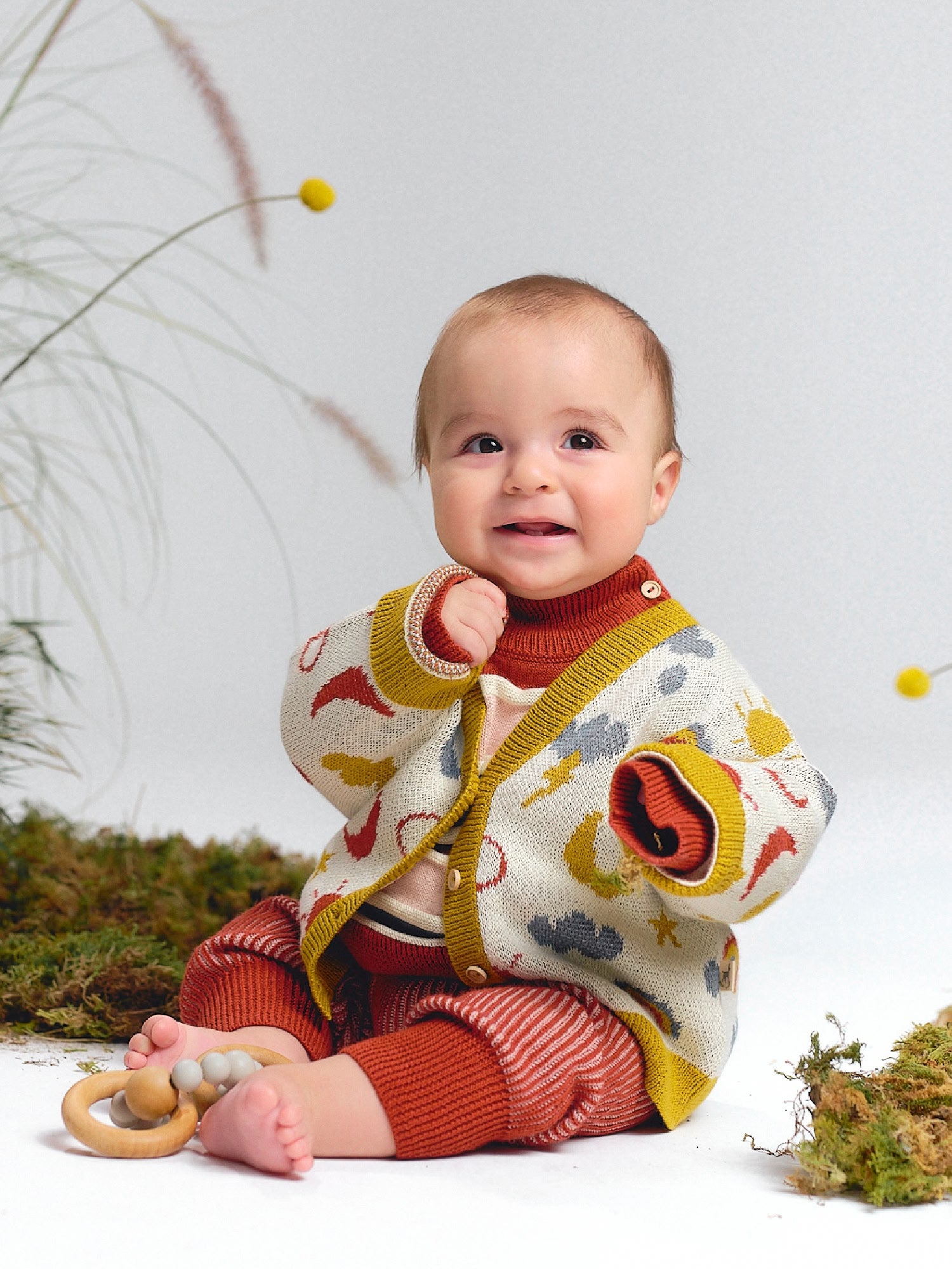 Multicolor knit cardigan with sky and weather motifs, paired with striped pants.