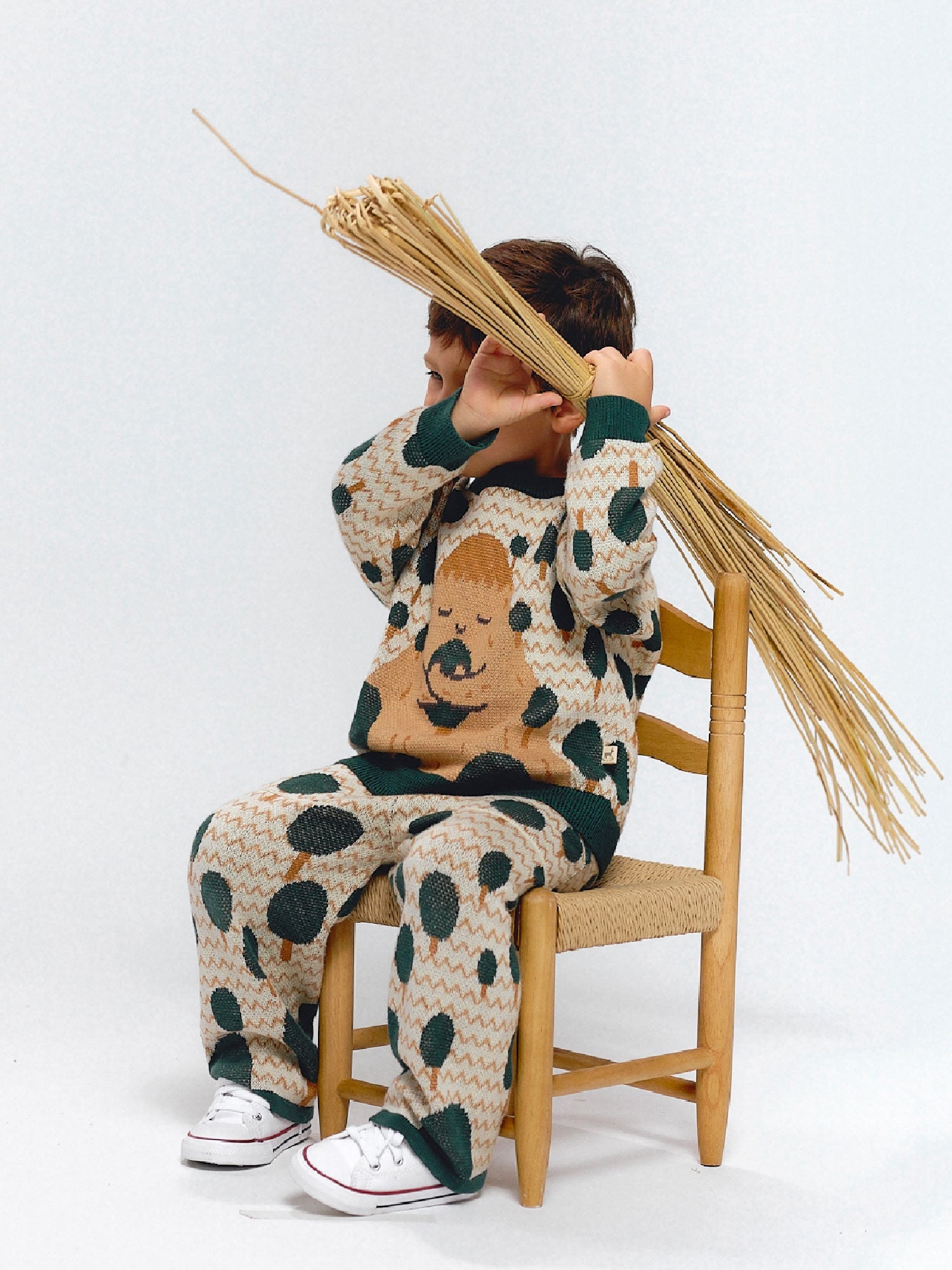 Child wearing a beige jacquard knit set decorated with green tree motifs inspired by mountains.