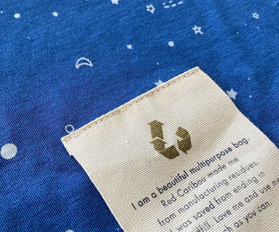 Close-up of blue fabric with star prints and a recycled label featuring the reuse symbol. Image from Red Caribou’s Upcycling Collection, crafted from recovered materials to reduce waste.